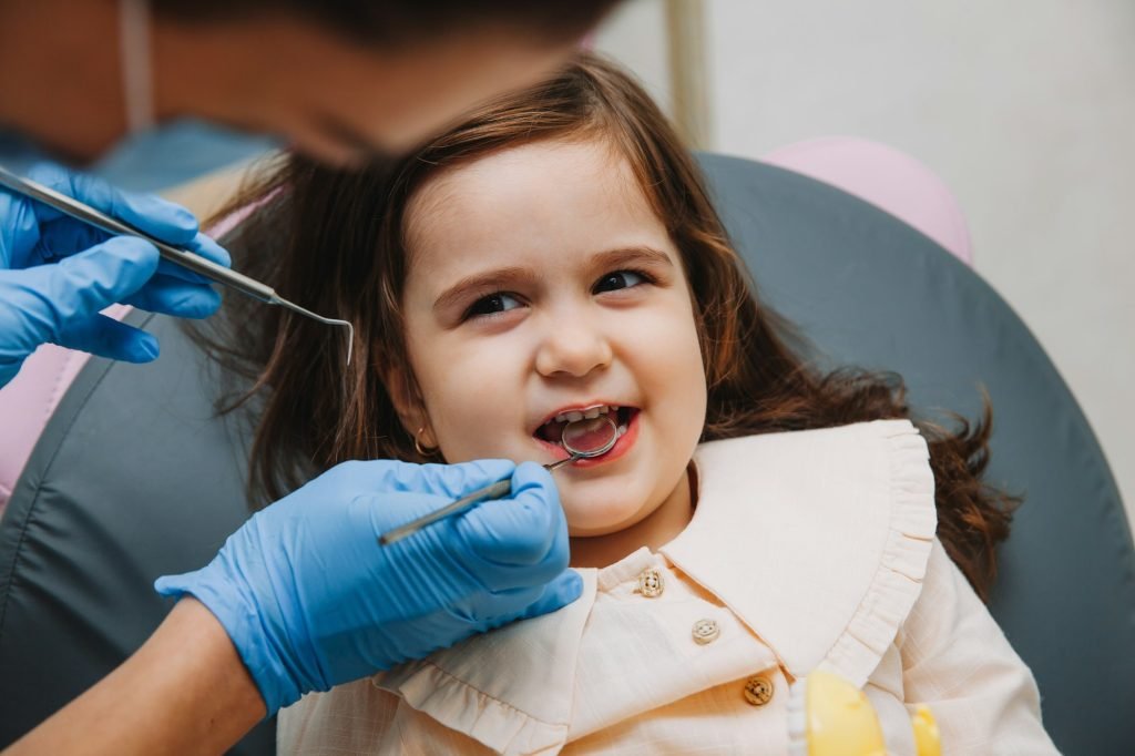 dentist, doctor examines the oral cavity of a little girl, uses a mouth mirror, baby teeth close-up,